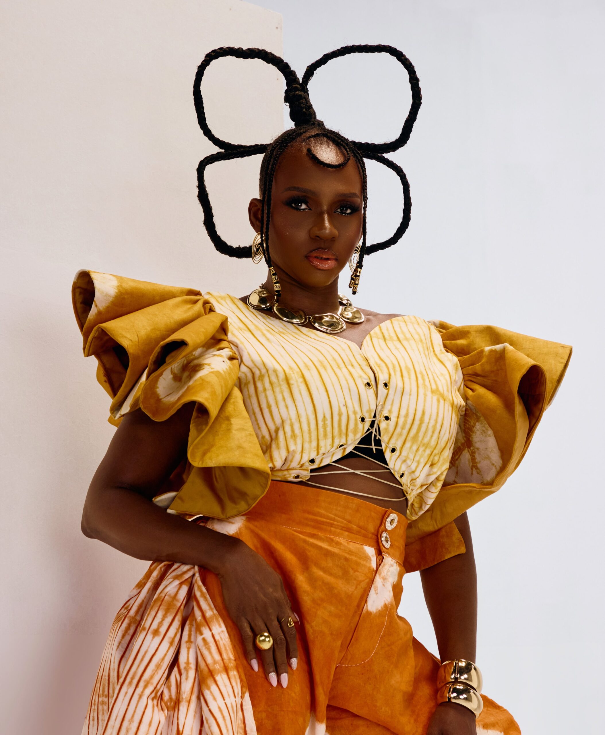 Singer Waje wearing a yellow tie-dye ruffled top and structured hairstyle with gold jewellery.