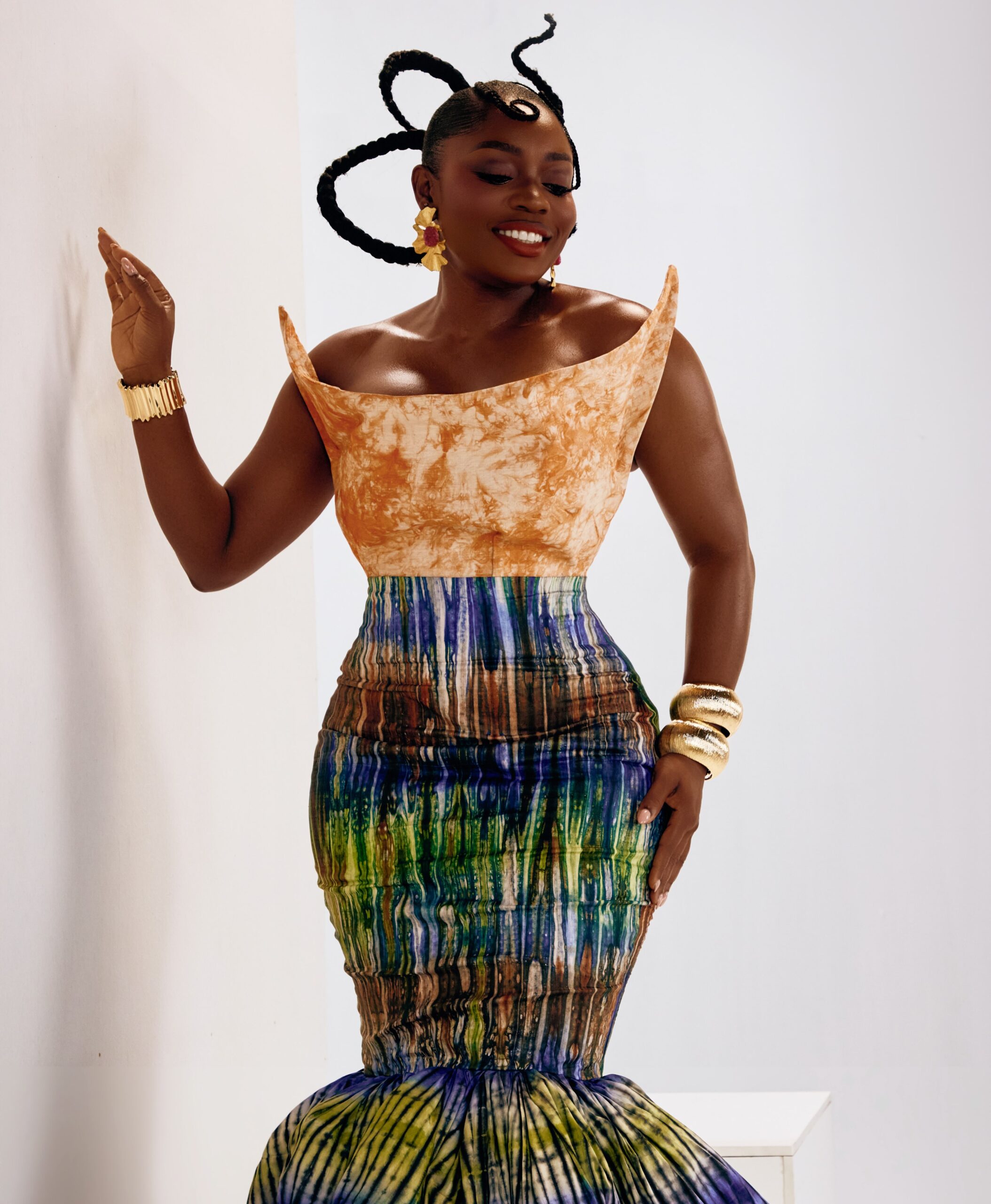 Bisola Aiyeola posing in an off-shoulder corset top and fitted patterned mermaid skirt with gold cuff bracelets.
