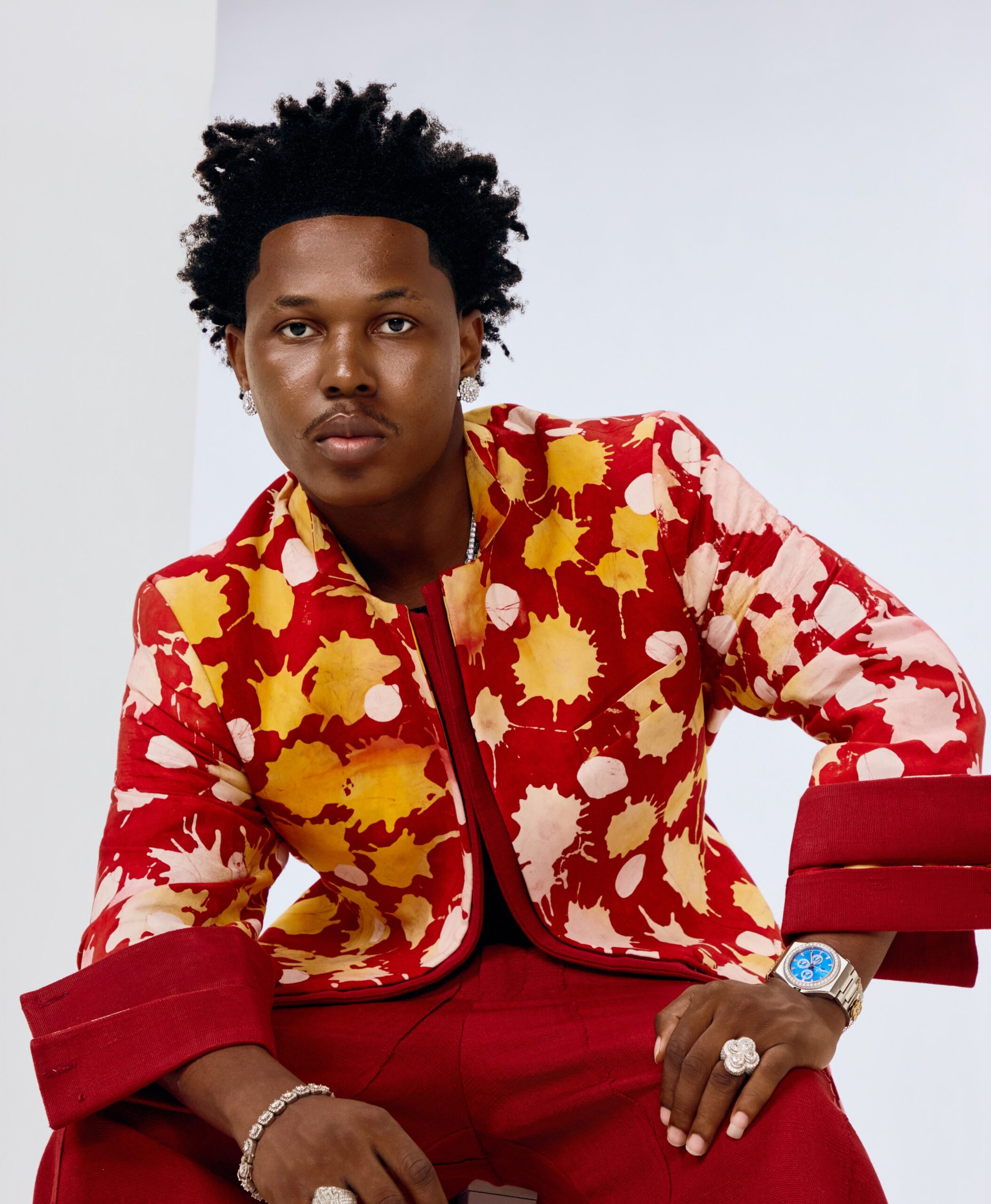 Afrobeats artist Shoday wearing a red and yellow splash-patterned jacket with matching red trousers.