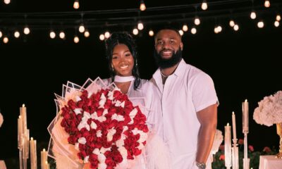 Meraiah Ekeinde in a white high-slit dress holding a red and white rose bouquet standing beside her fiancé Manny in all-white