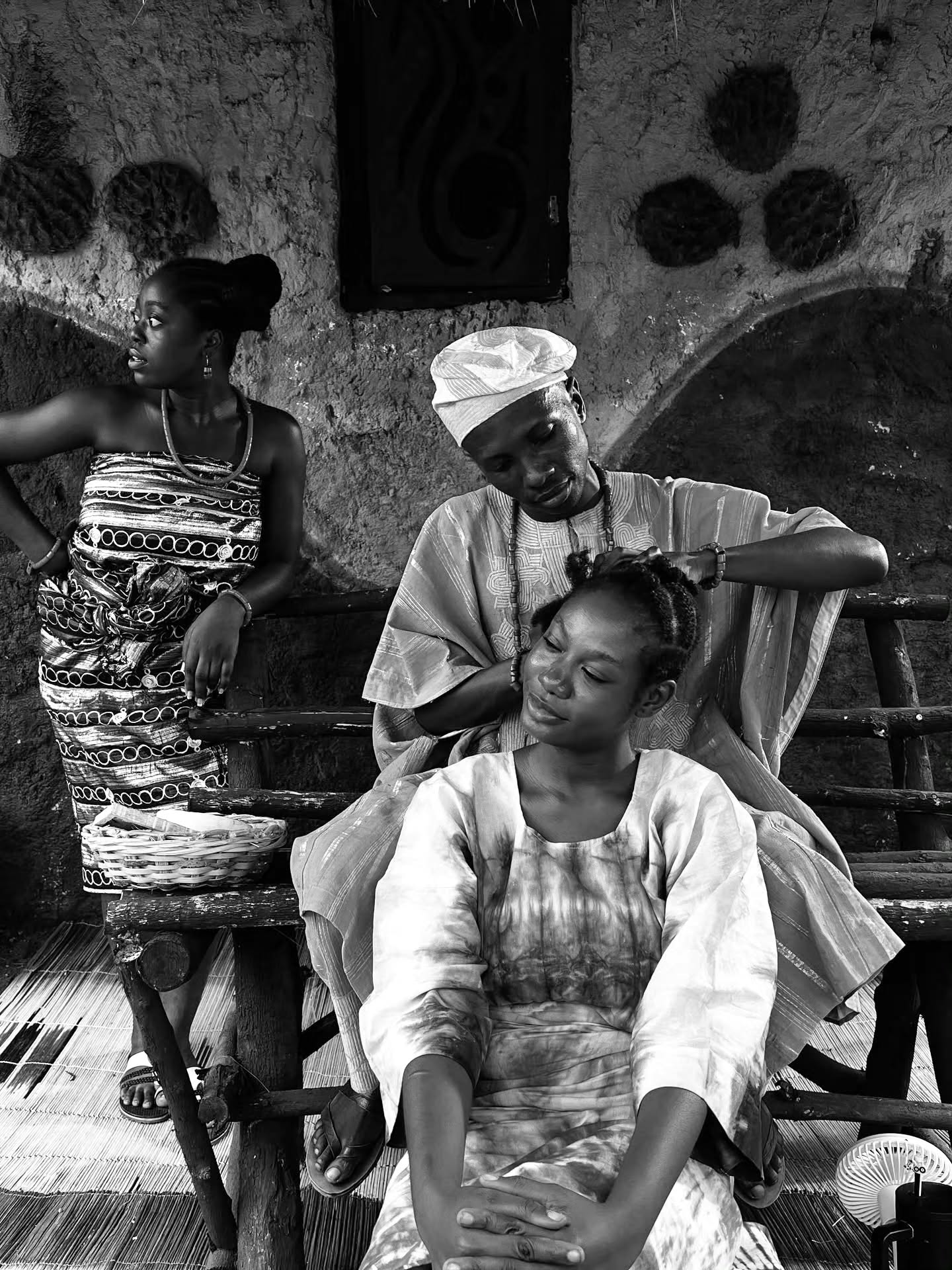 Black and white photo of Moshood Fattah weaving Tomi Ojo's hair on the set of Alahun The Weaver.