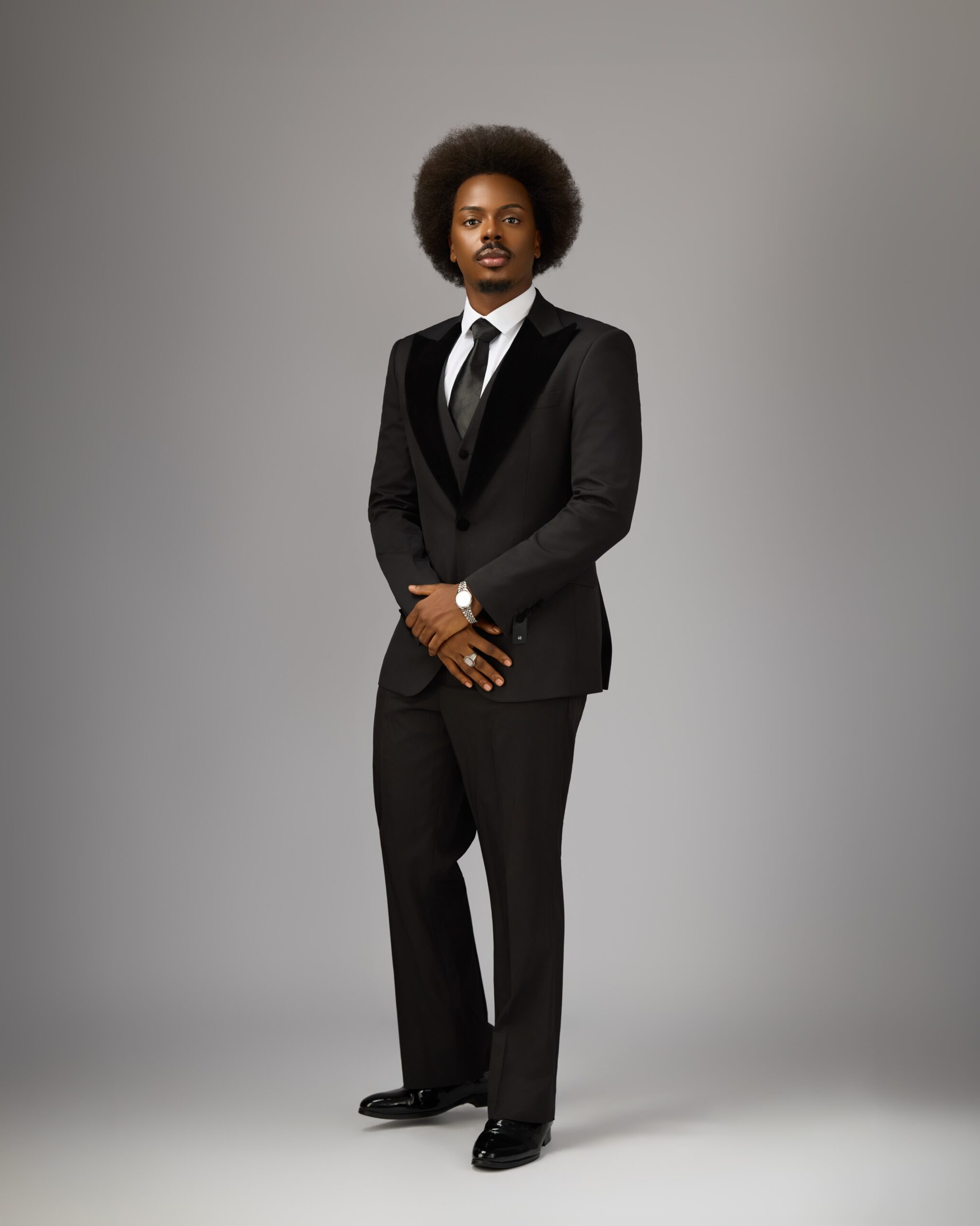 Full-length photo of Enioluwa Adeoluwa in a black three-piece tuxedo and patent leather shoes.