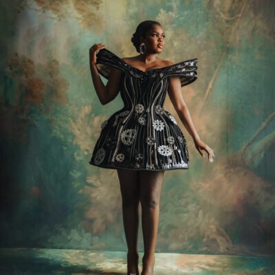 Jarvis posing solo in a black A-line mini dress adorned with gears, cogs, spanners, and exposed zips.