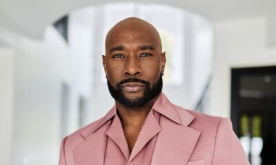 Morris Chestnut wearing a rose pink jacket with wide peak lapels, a luxury wristwatch, and a trimmed dark beard.