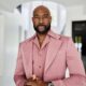 Morris Chestnut wearing a rose pink jacket with wide peak lapels, a luxury wristwatch, and a trimmed dark beard.