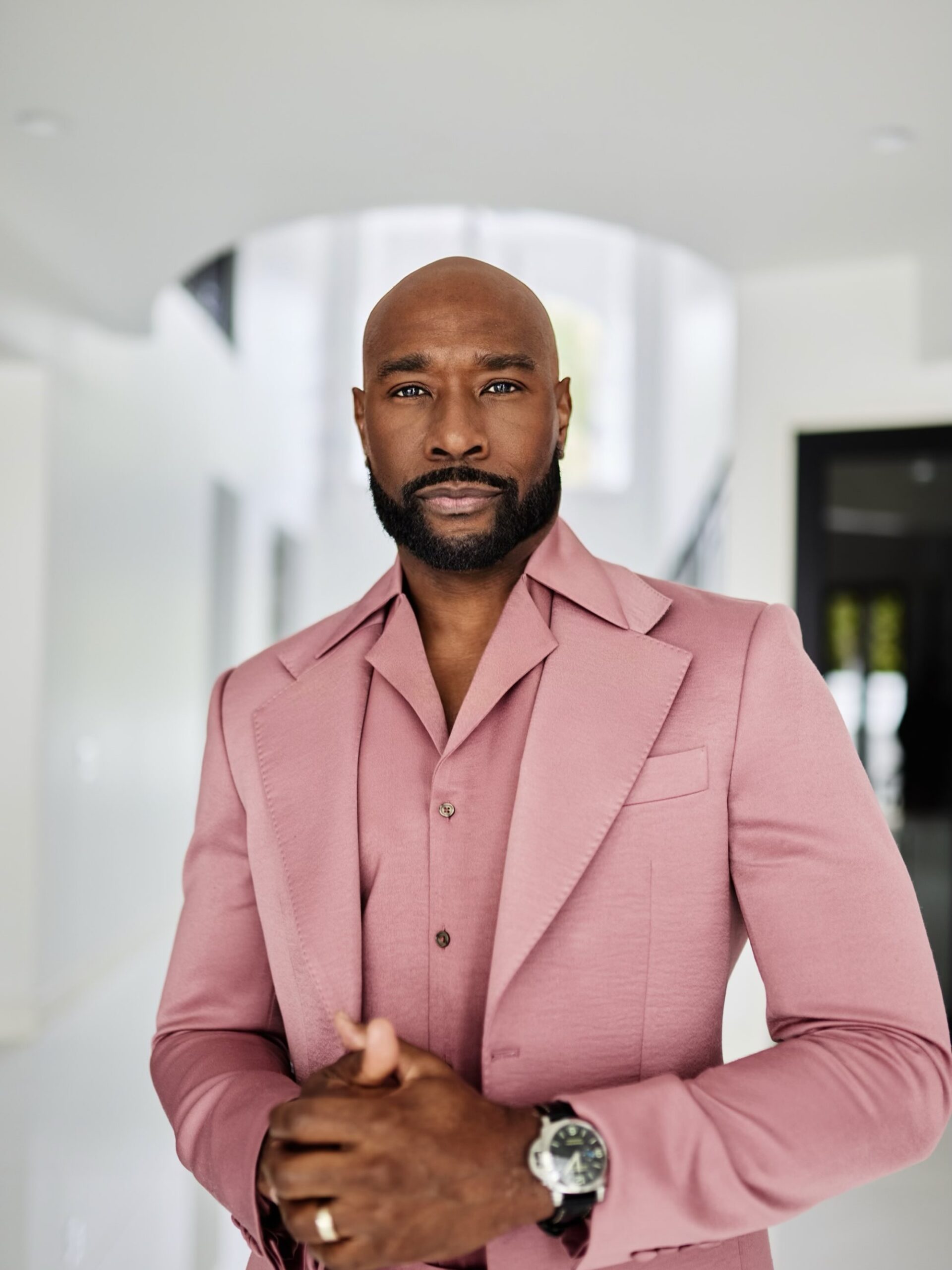 Morris Chestnut wearing a rose pink jacket with wide peak lapels, a luxury wristwatch, and a trimmed dark beard.