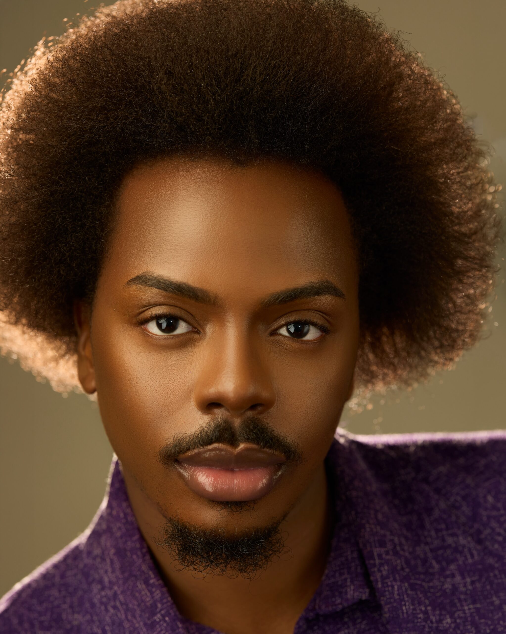 headshot of Enioluwa Adeoluwa showcasing a rounded Afro and trimmed goatee in a textured purple shirt.