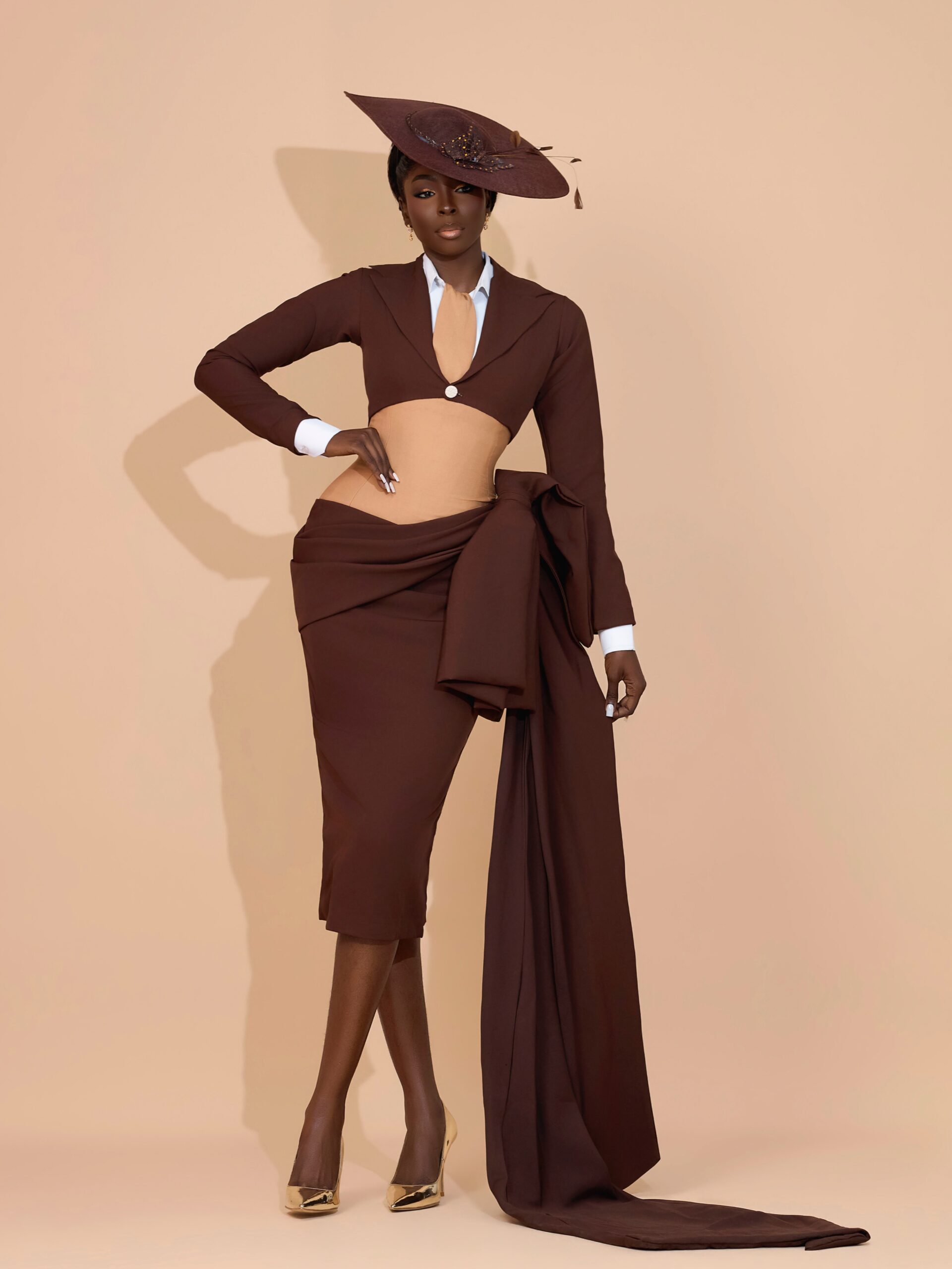 Tamunosoye Karibi-George in a brown structured cropped jacket, matching skirt with a side drape, white collar, tie, and brown hat.