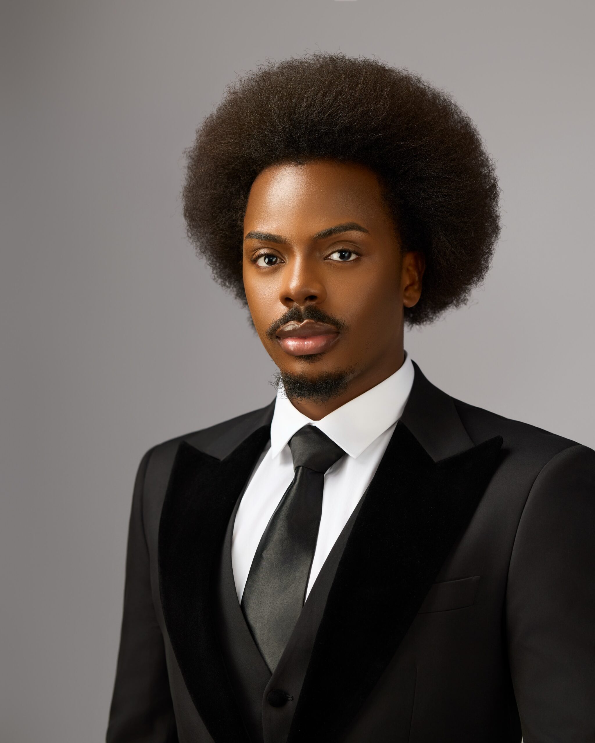 Close-up headshot of Enioluwa Adeoluwa wearing a black tuxedo with velvet lapels and a satin tie.
