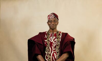 Full-length studio portrait of Adedimeji Lateef in a wine three-piece Agbada set, black velvet loafers, and coral jewellery.