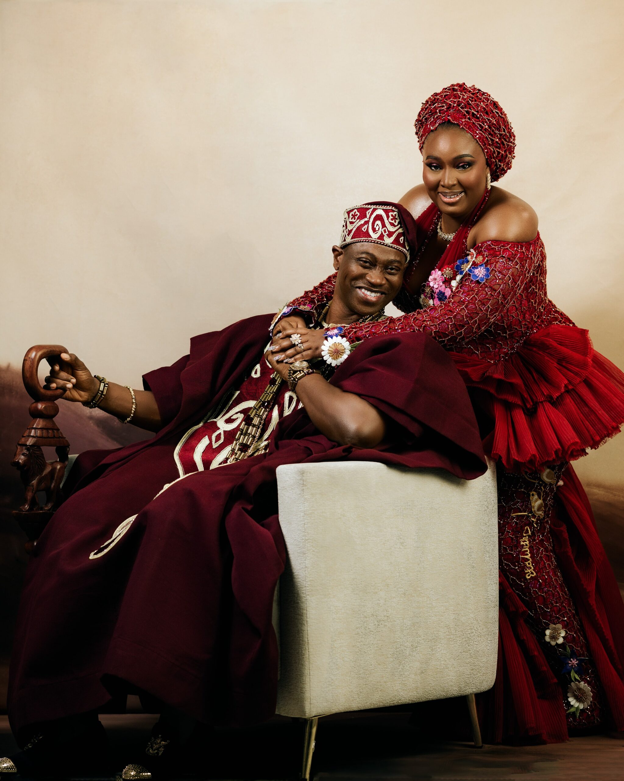 Mo Bimpe smiling as she leans over her seated husband, Lateef Adedimeji, in coordinated burgundy lace and agbada attire.