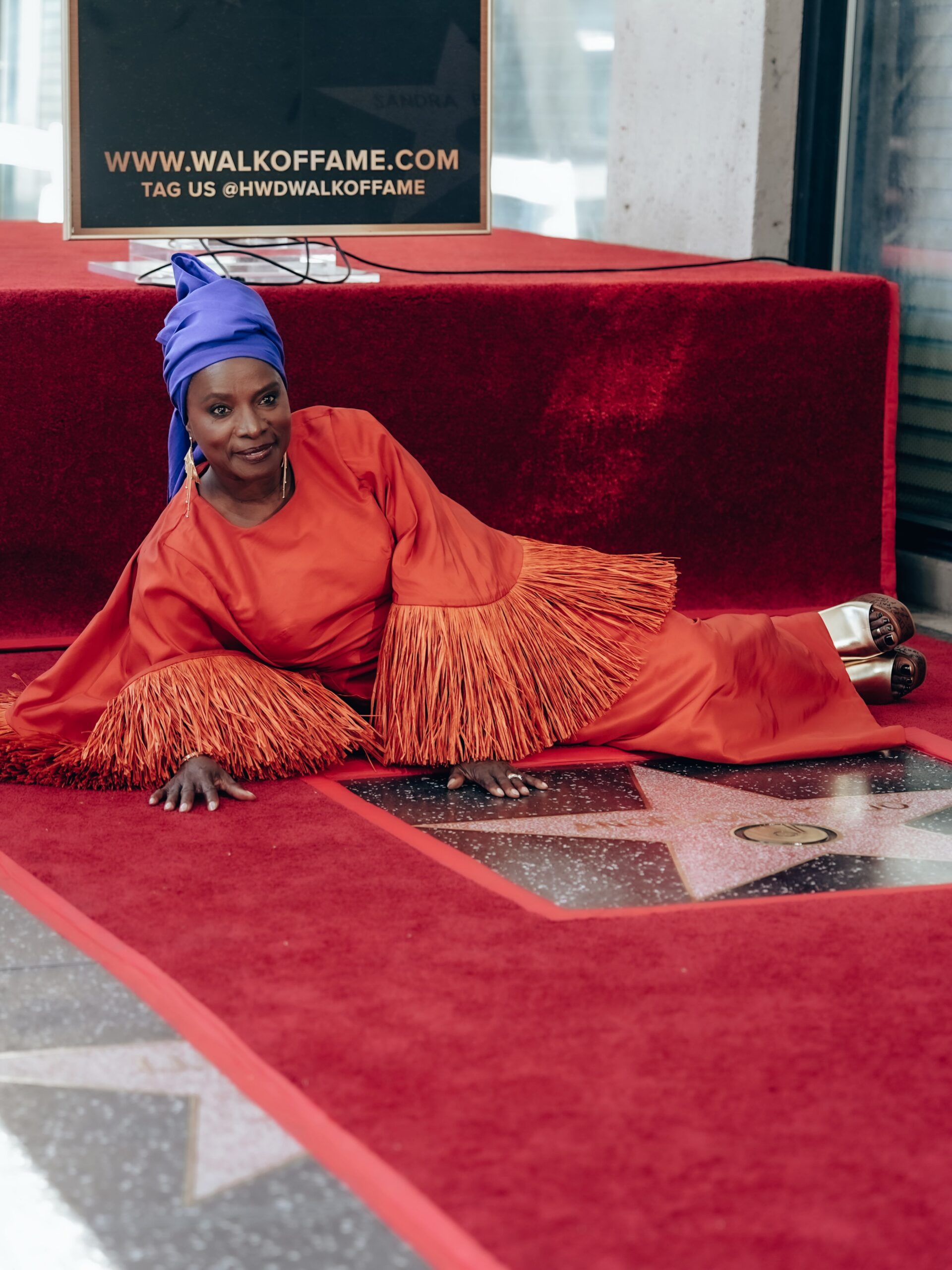 Angélique Kidjo reclining on the red carpet next to her Hollywood Walk of Fame star plaque