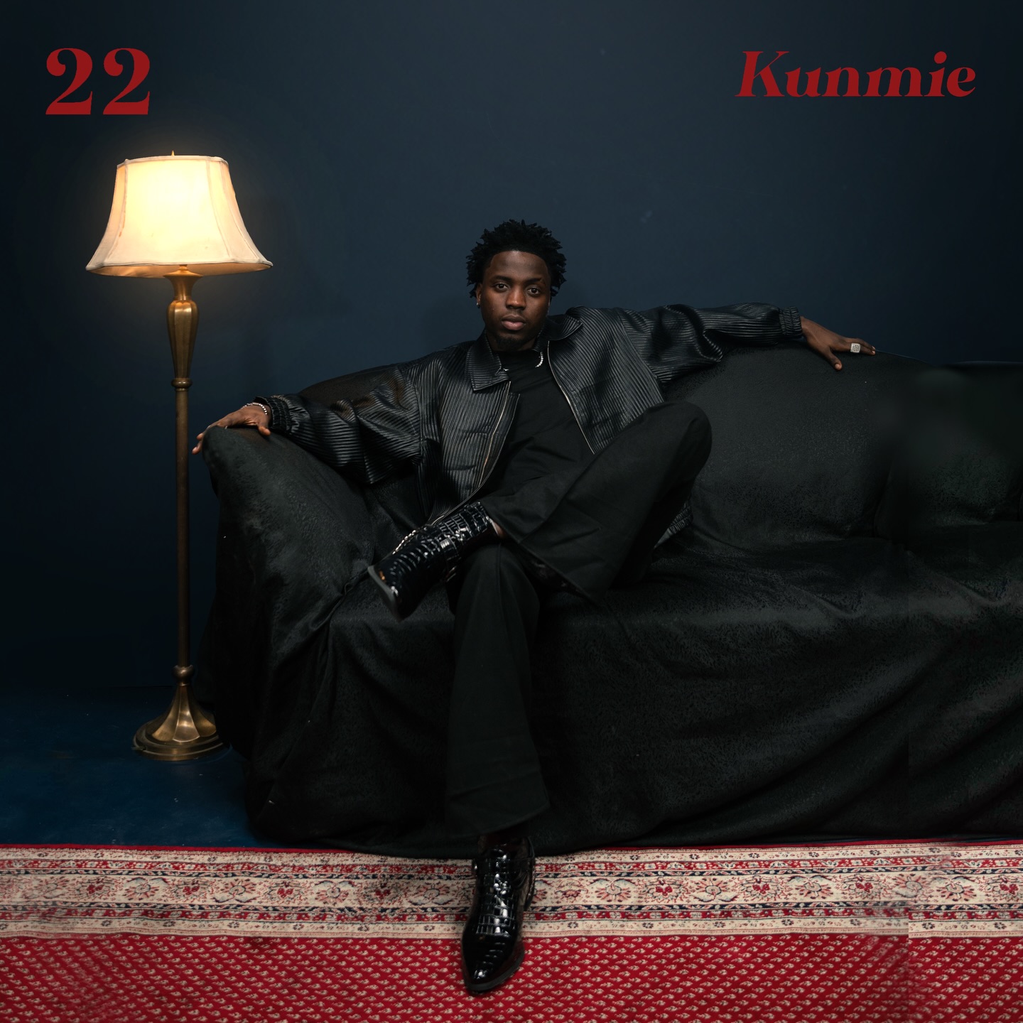 Kunmie sitting on a black sofa next to a floor lamp for his debut album 22