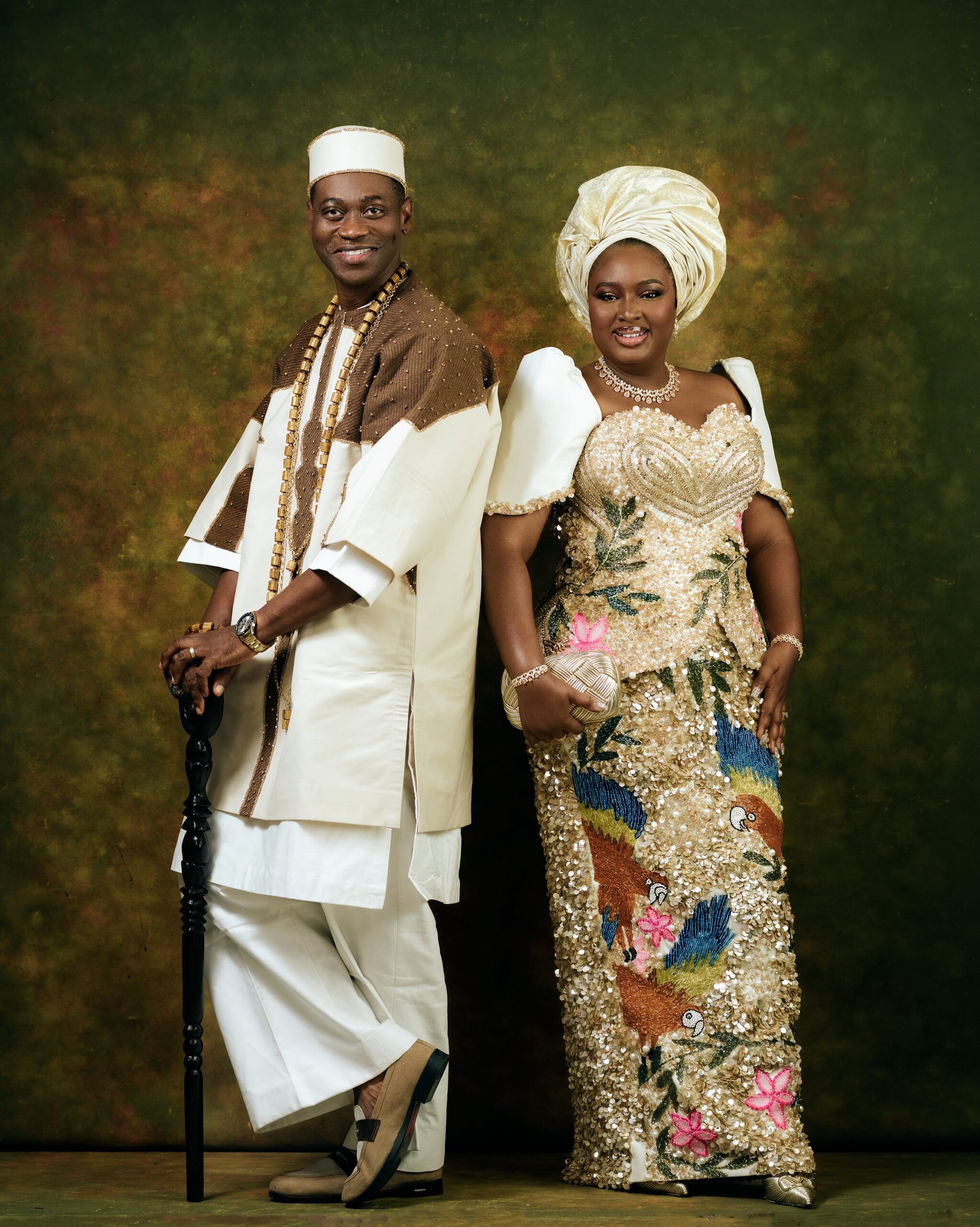Lateef Adedimeji and Mo Bimpe posing back-to-back in cream and gold traditional outfits against a vintage olive background.