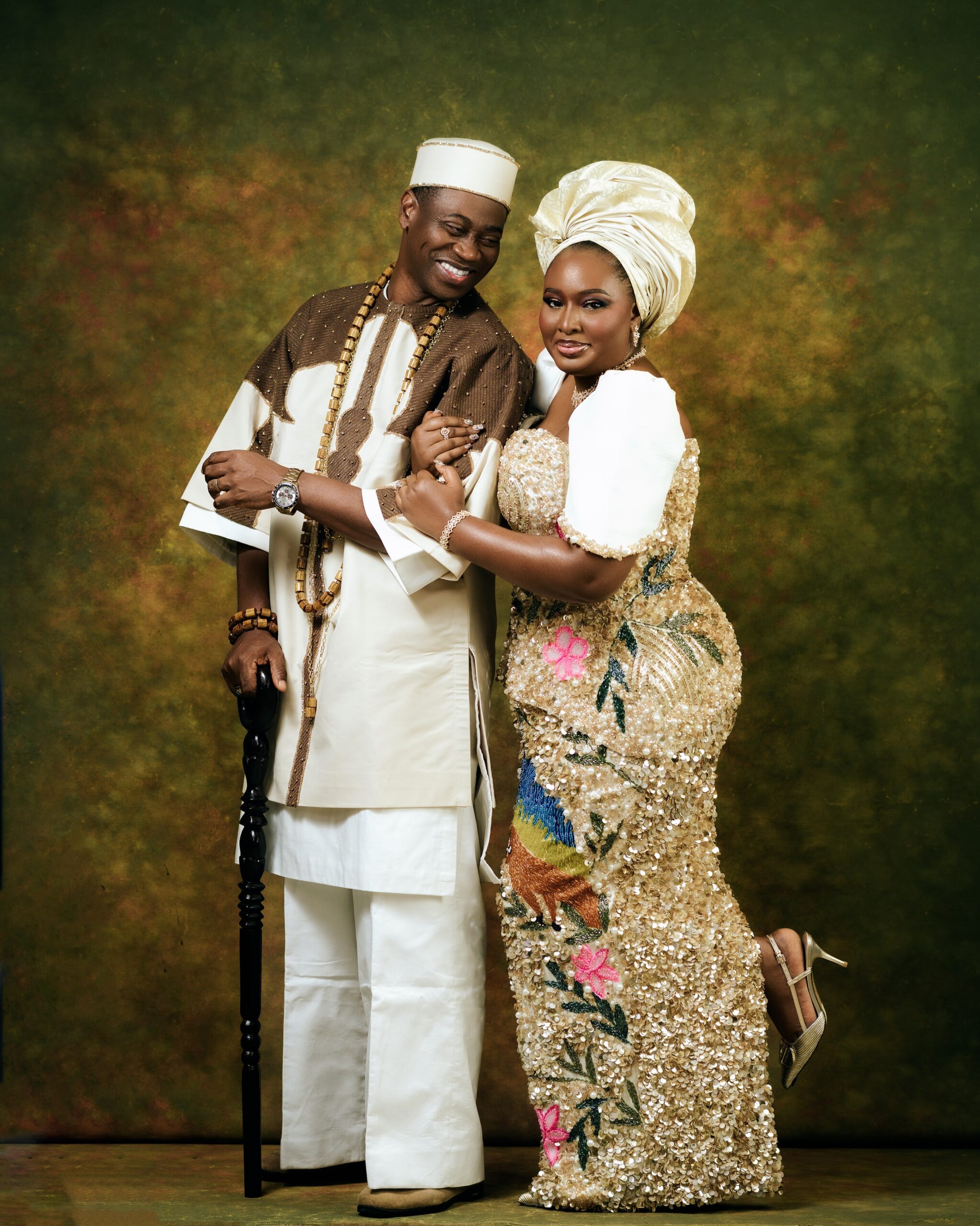Mo Bimpe holding Lateef Adedimeji’s arm while looking forward in gold and cream traditional Nigerian attire.