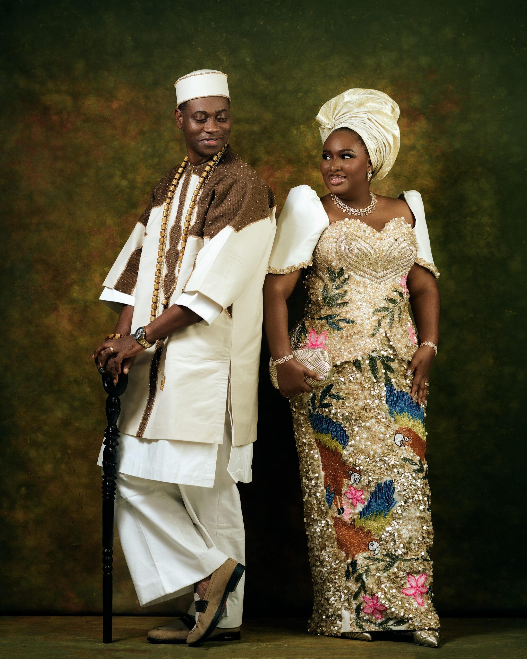 Lateef Adedimeji leaning on a dark walking stick and looking at Mo Bimpe in her champagne-gold sequined gown.