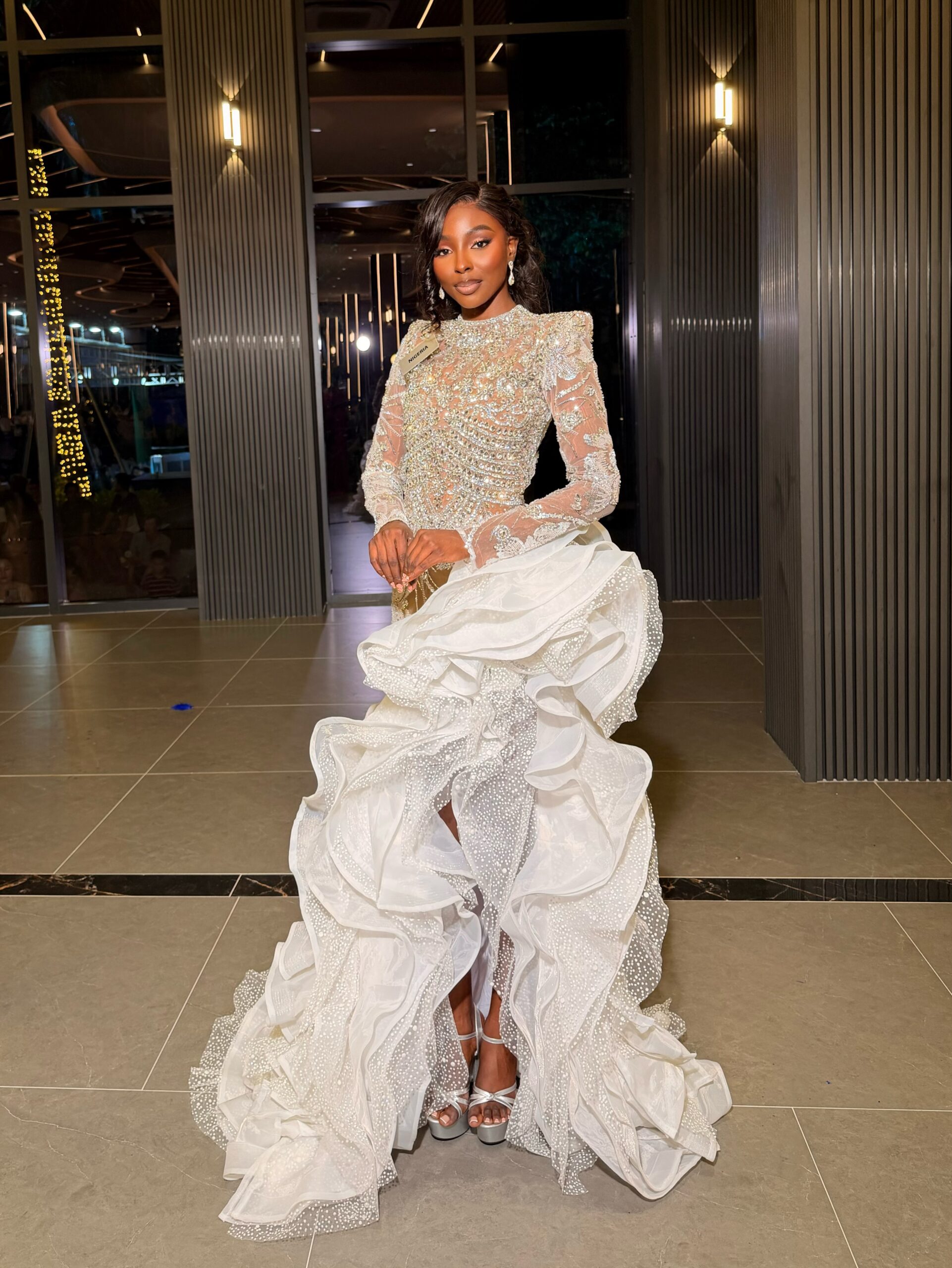 Tamunosoye Karibi-George posing in a sheer high-neck white embellished evening gown with layered ruffle skirt detail.