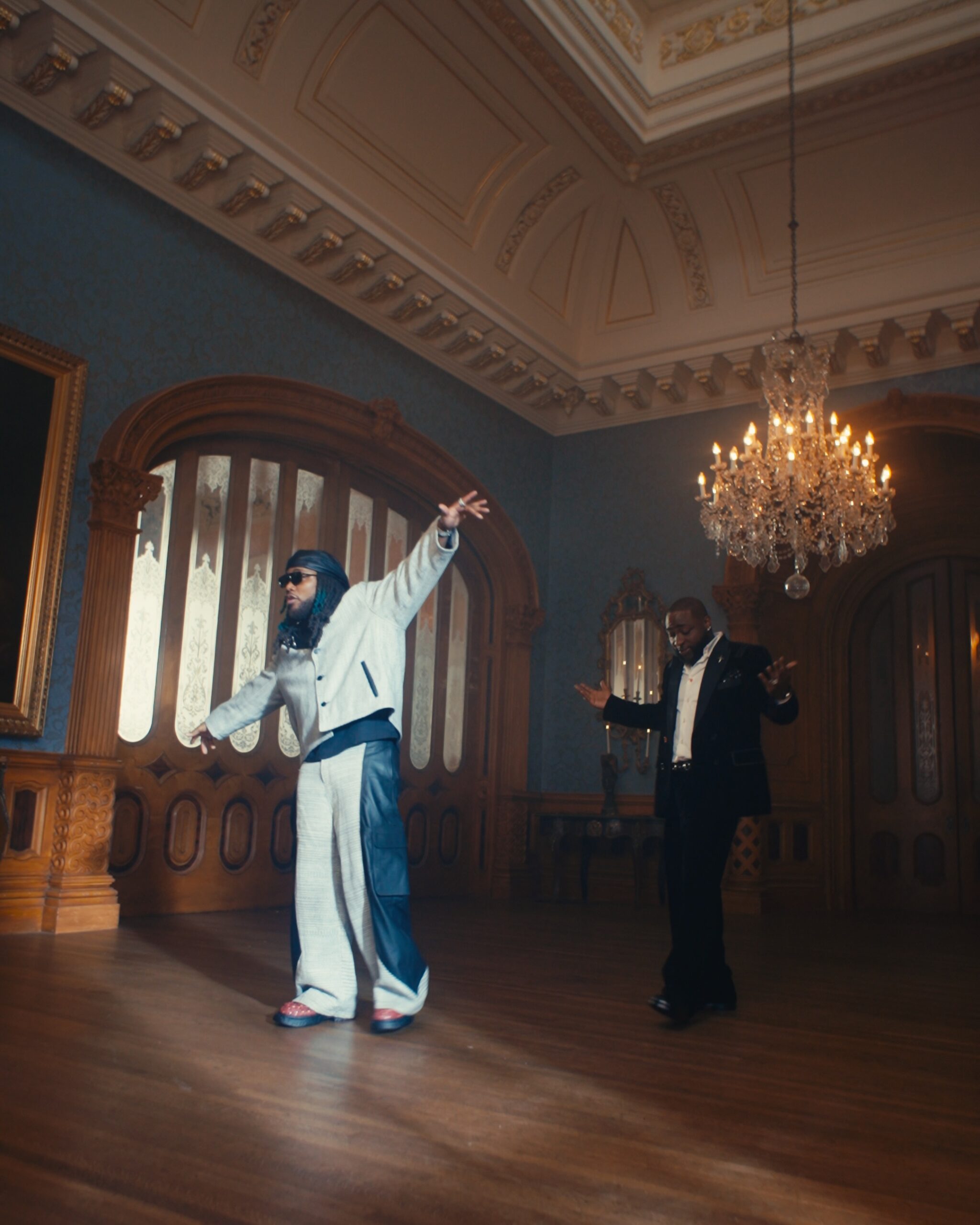 Davido and Leon Thomas dancing inside a luxury mansion hall in the Tell Everybody video.