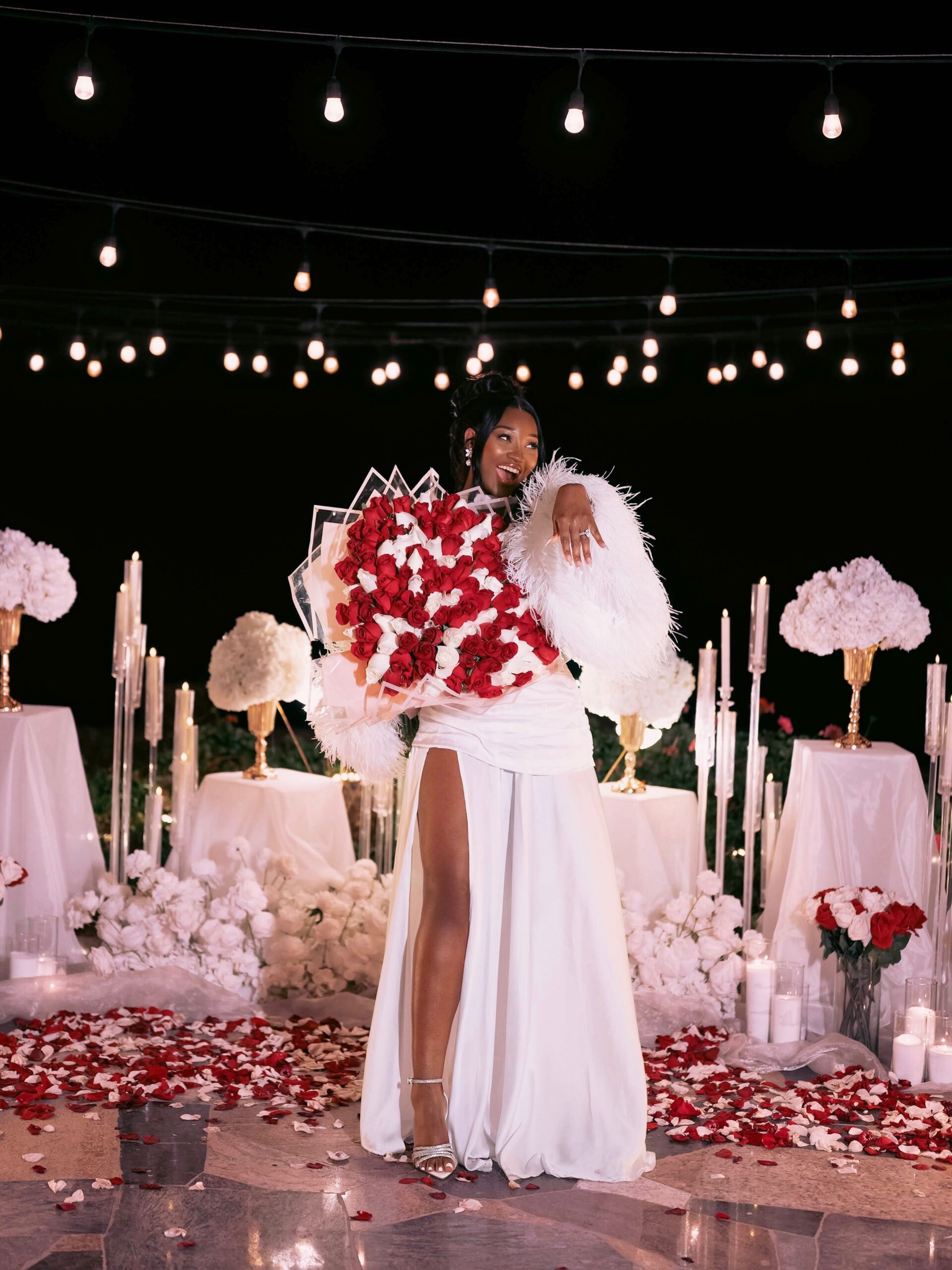 Meraiah Ekeinde posing solo in a white feather-trimmed dress showing off her engagement ring while holding a rose bouquet
