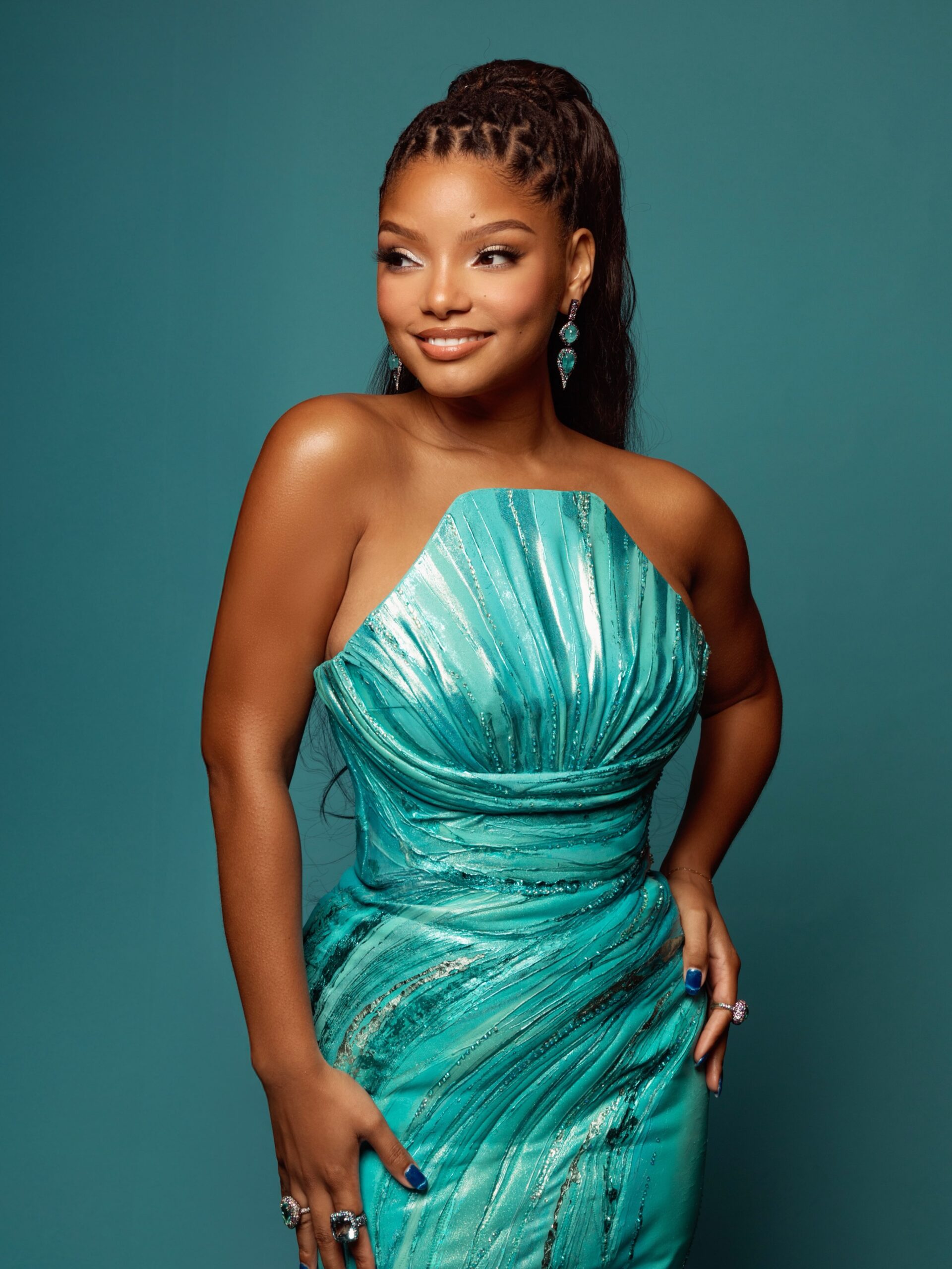 Halle Bailey posing in a strapless metallic teal Valdrin Sahiti dress with shell pleated bust.