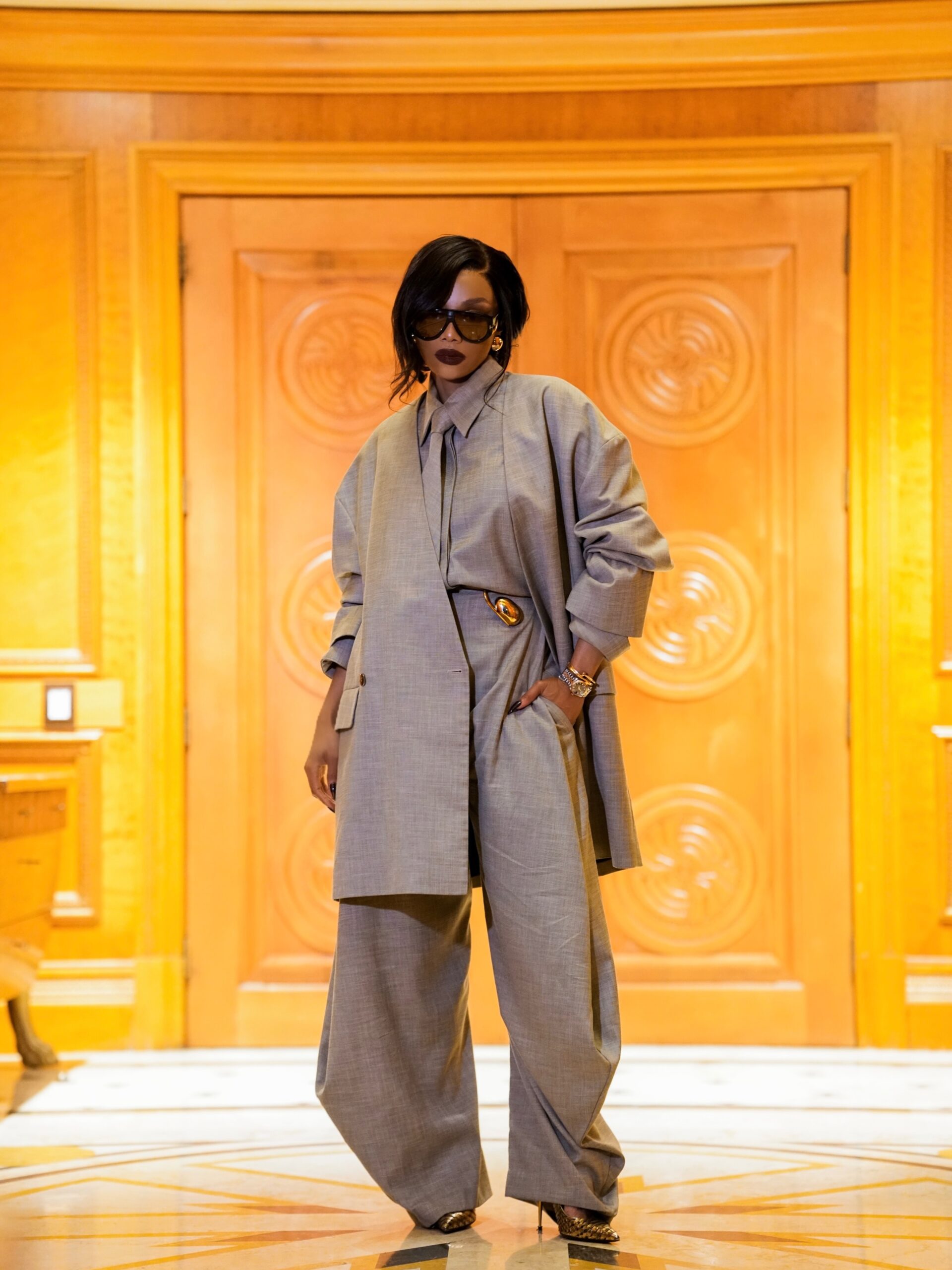 Bonang Matheba posing in an oversized grey suit with a gold waist buckle.