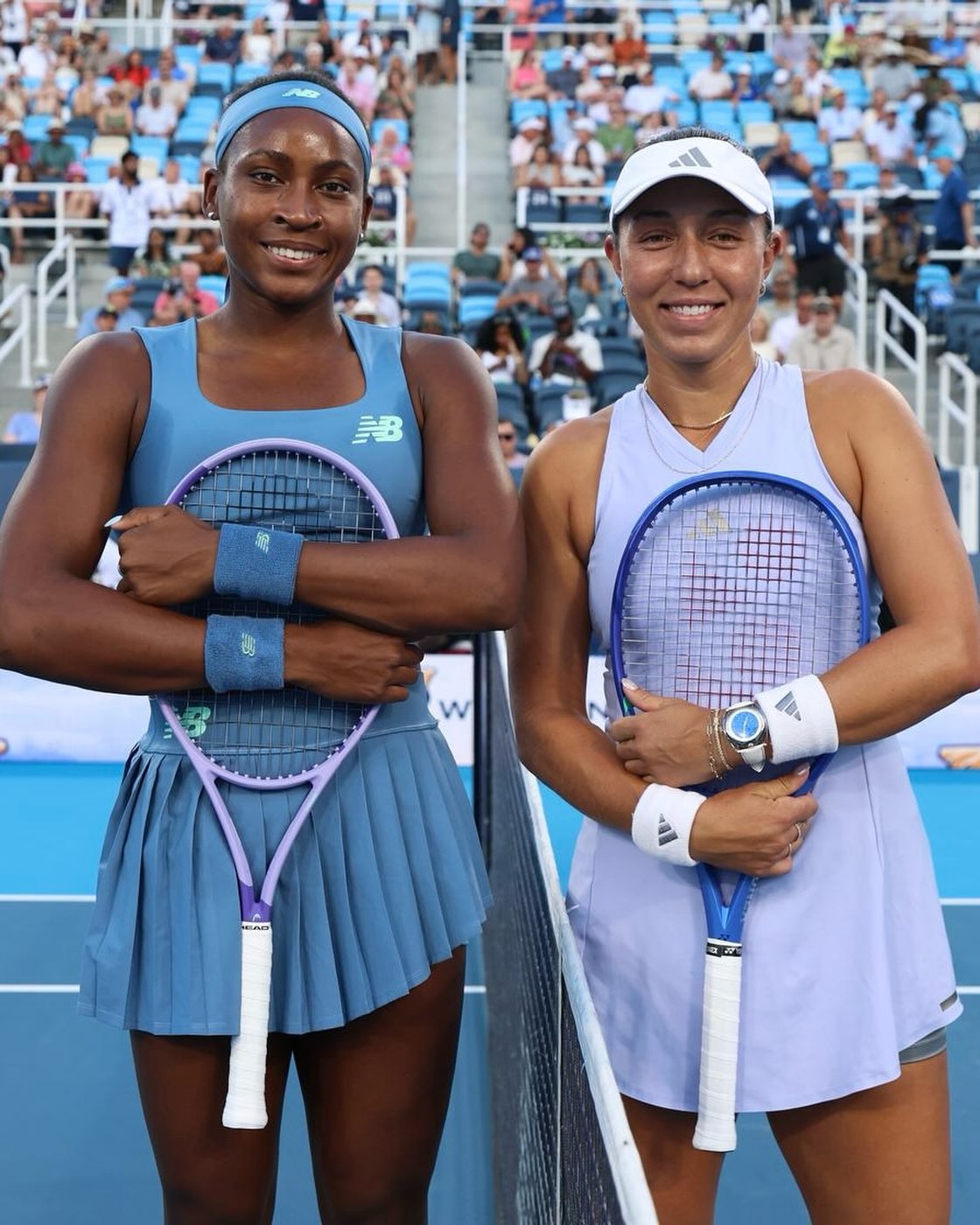 Coco Gauff and Jessica Pegula posing together with tennis rackets at the net