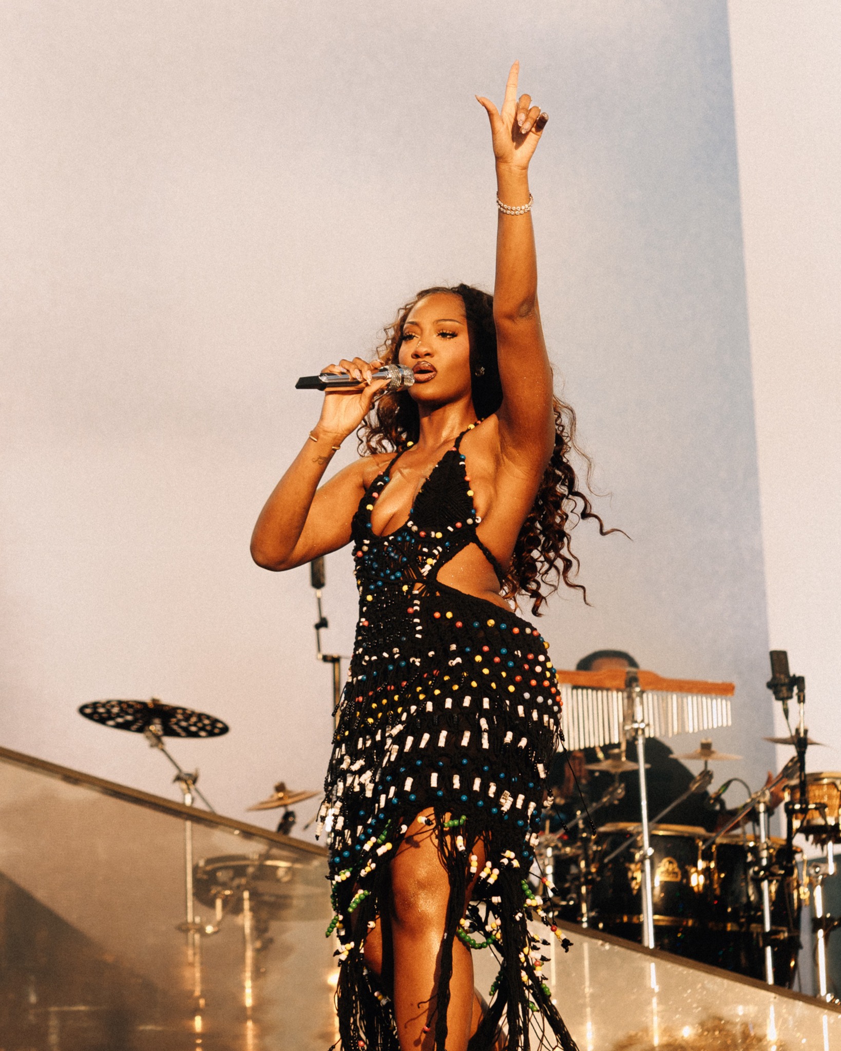 Tems singing on stage in a black beaded MIO crochet dress at Victoria Park London.