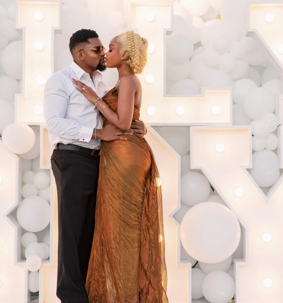Diana Eneje kissing her fiancé in front of white balloons and illuminated marquee letters.