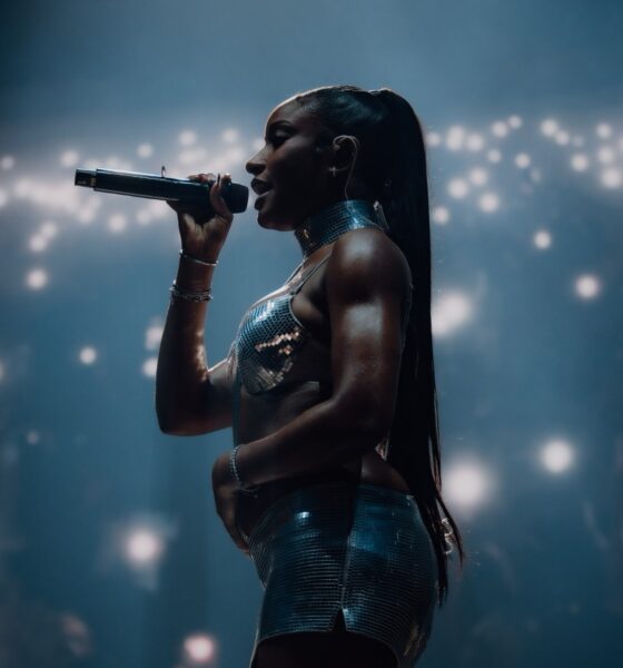 Ayra Starr performing live on stage at All Points East 2026 festival holding a microphone in a metallic silver two-piece outfit with a sleek ponytail.