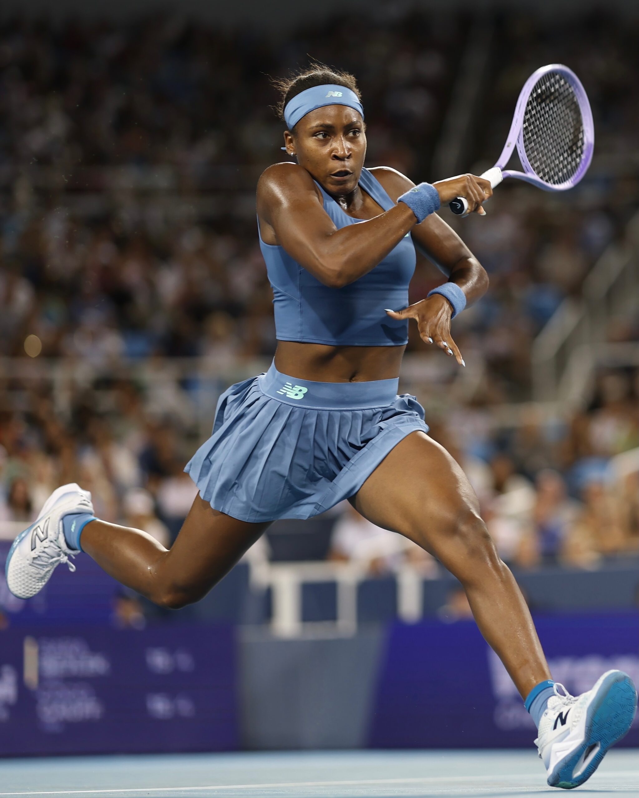 Coco Gauff hitting a backhand stroke in a light blue pleated skirt at the Cincinnati Open.