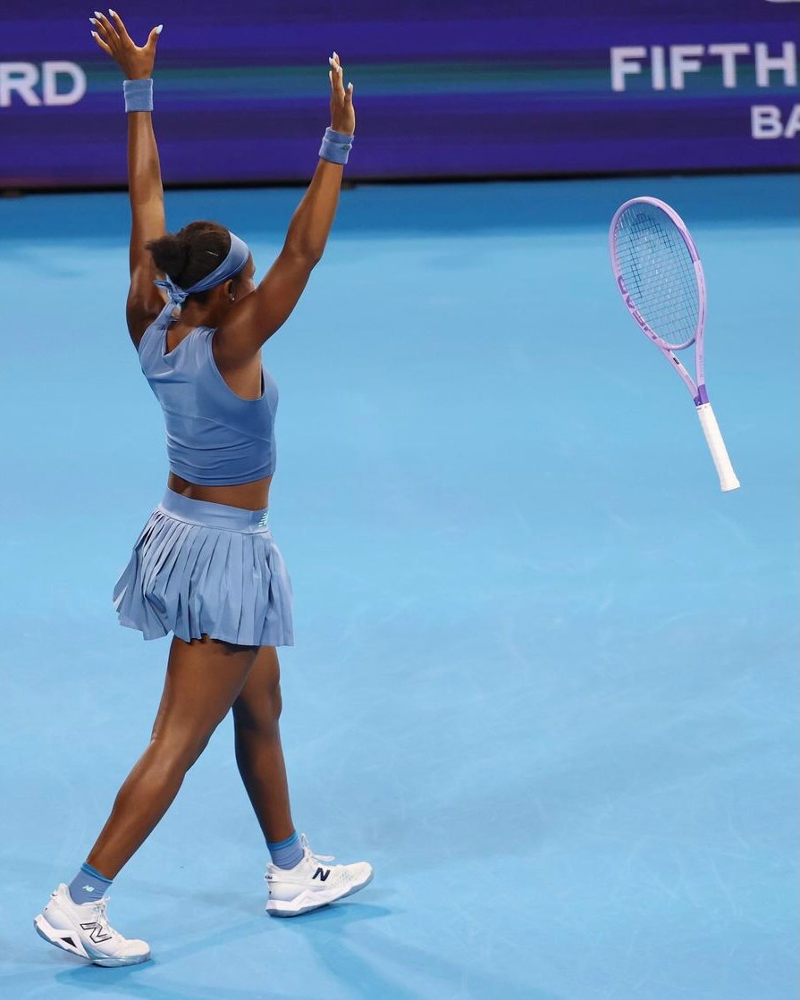 Coco Gauff throwing her tennis racket into the air with arms raised in victory