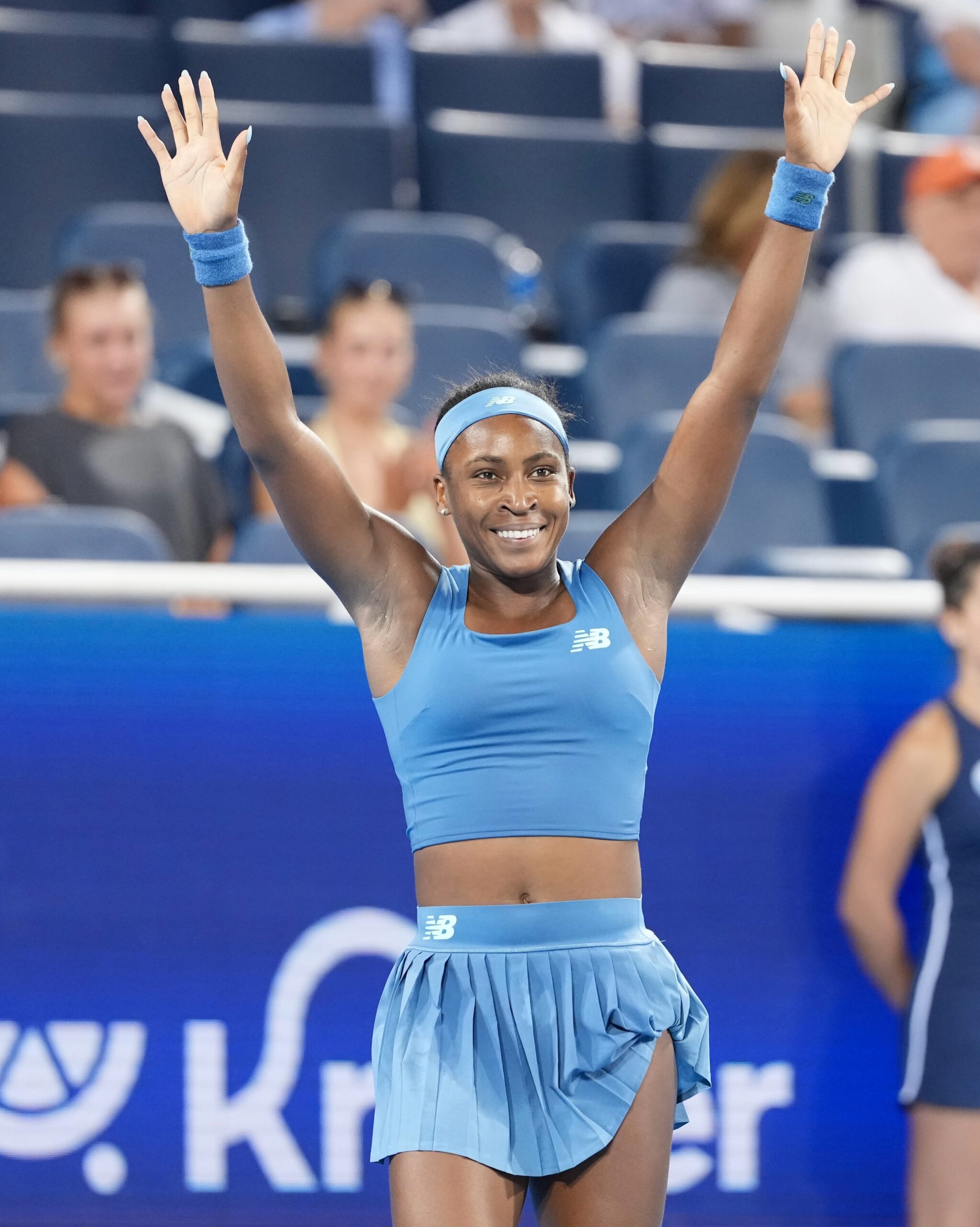 Coco Gauff smiling with both hands raised to applaud the court crowd