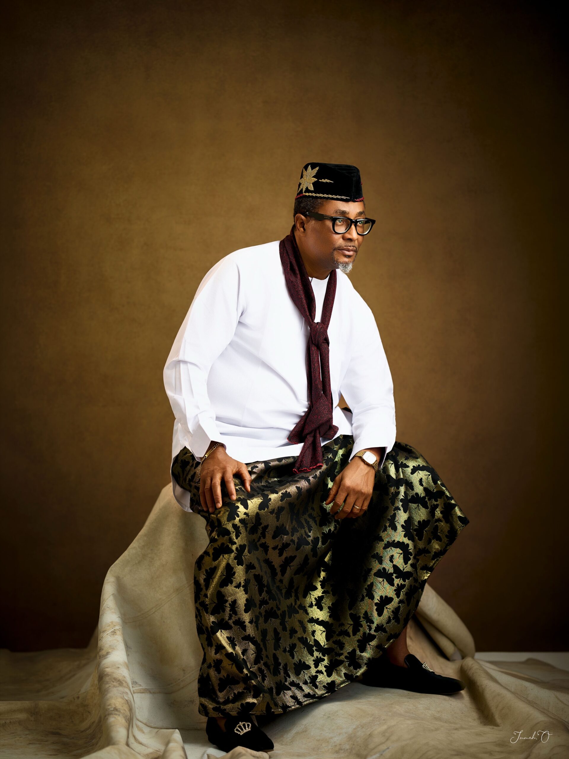 Nollywood actor Tony Umez in a white tunic, gold and black wrapper, and maroon scarf for his 60th birthday photoshoot.