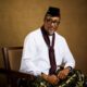 Tony Umez wearing a black embroidered cap, white tunic, and maroon scarf.