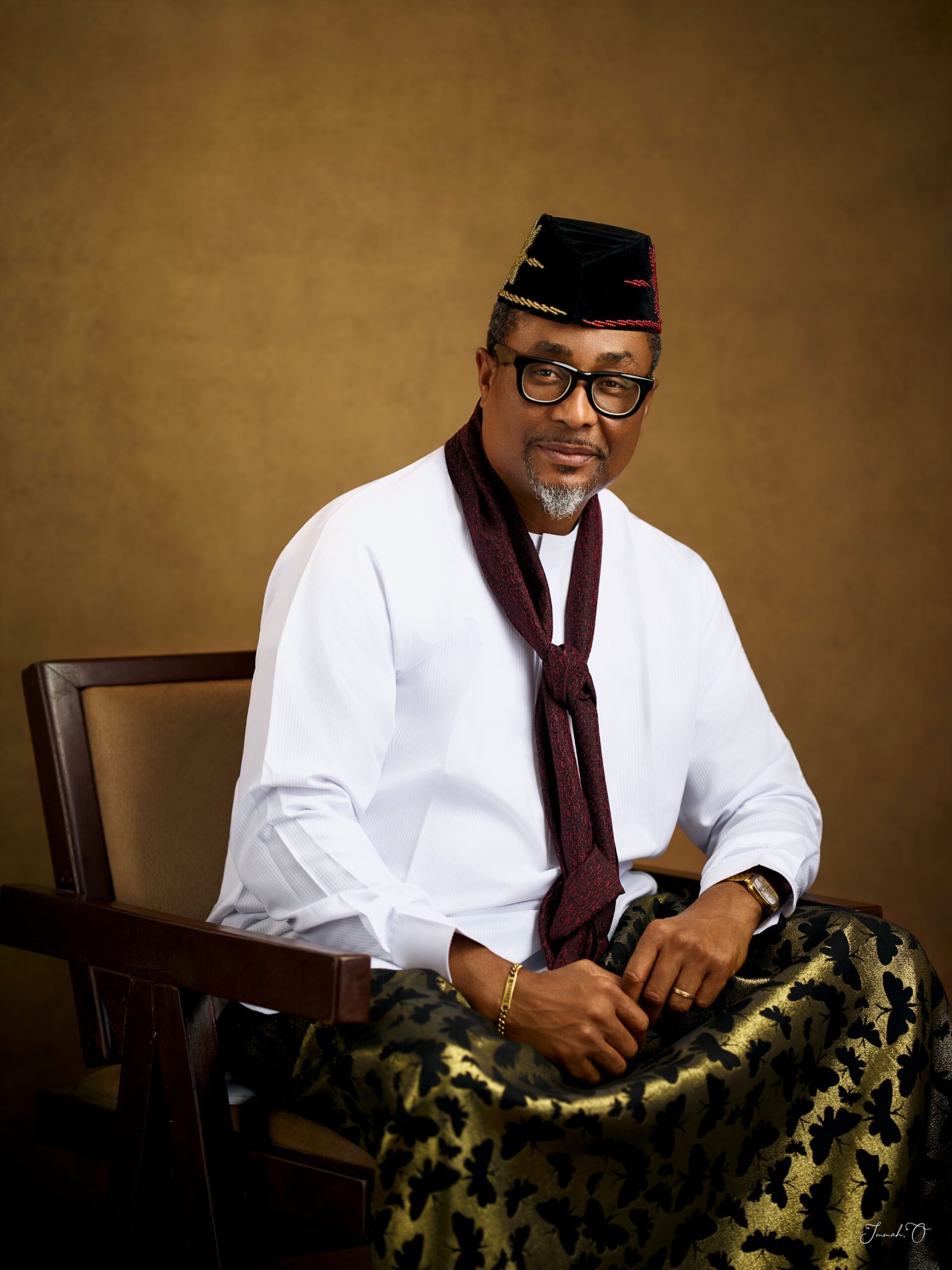 Tony Umez wearing a black embroidered cap, white tunic, and maroon scarf.