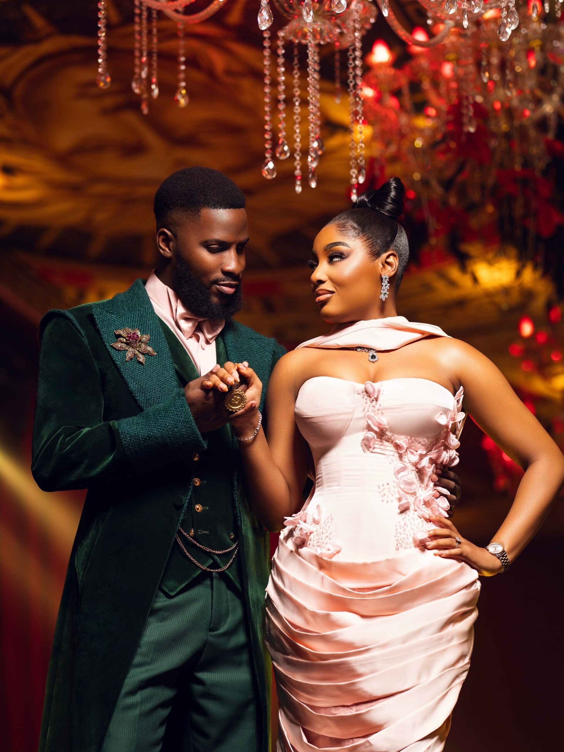 Akin Faminu holding hands with Kiky Festus, featuring his floral brooch and her embellished blush pink gown.