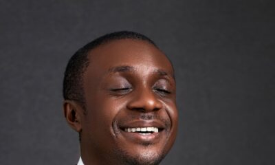 Nathaniel Bassey smiling with eyes closed while wearing a black suit jacket, white shirt, and dark tie for his 45th birthday.