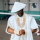 Ebuka Obi-Uchendu wearing a white pleated Japanese hat, gold-rimmed sunglasses, coral beads, and holding a blonde horsetail whip.