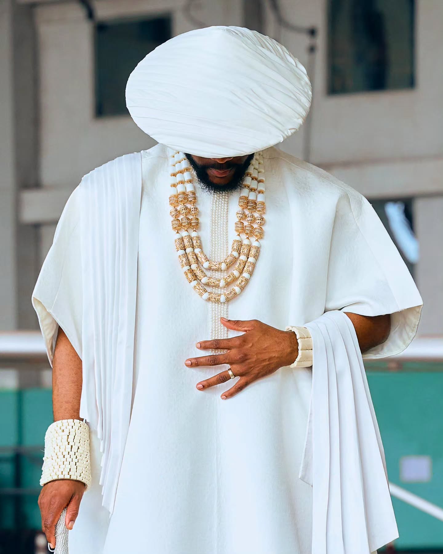 Ebuka Obi-Uchendu wearing heavy multi-strand coral and gold neckbeads over a white Japanese-inspired tunic with a pleated Japanese hat.