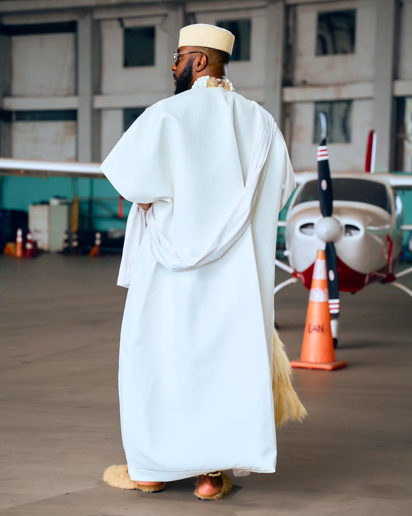 Rear view of Ebuka Obi-Uchendu wearing a white Ugo Monye Japanese-inspired robe with a structured cream cap and fur mules.