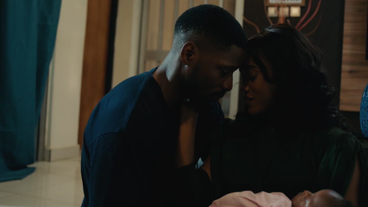 Tobi Bakre and Onyinye Odokoro leaning heads together while holding their sleeping baby in Before We Fall Asleep.