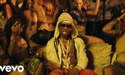 Mavin Records artist Rema wearing a pattern-patterned hooded jacket, sunglasses, and layered gold butterfly necklaces in a scene from his official TEA music video.