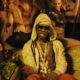Mavin Records artist Rema wearing a pattern-patterned hooded jacket, sunglasses, and layered gold butterfly necklaces in a scene from his official TEA music video.