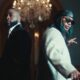 Davido in a black suit and Leon Thomas in a cream jacket standing back-to-back in the Tell Everybody music video.