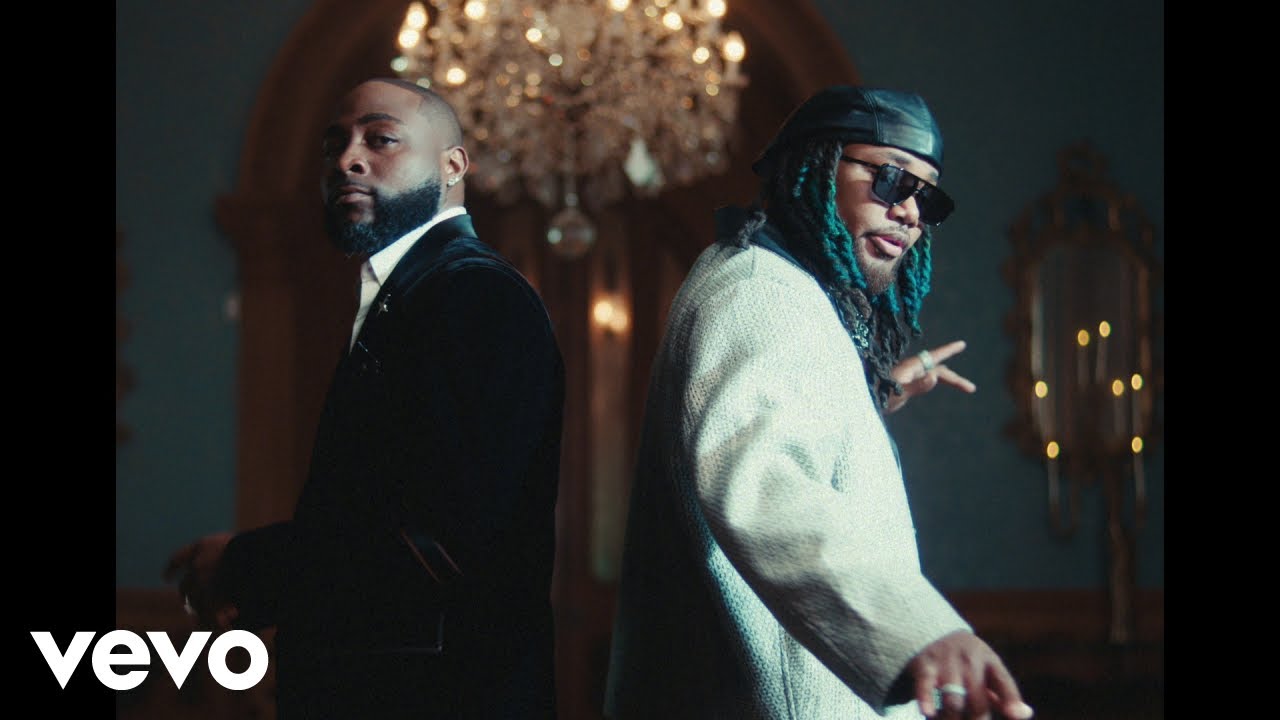 Davido in a black suit and Leon Thomas in a cream jacket standing back-to-back in the Tell Everybody music video.