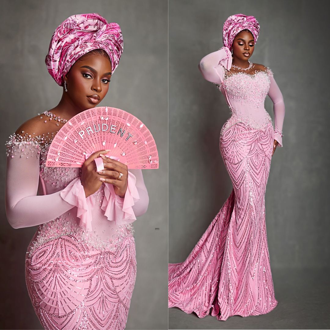 Prudent Gabriel wearing a pink mermaid gown with sheer long sleeves, shoulder beadwork, and a structured Gele at Akin Faminu traditional wedding.