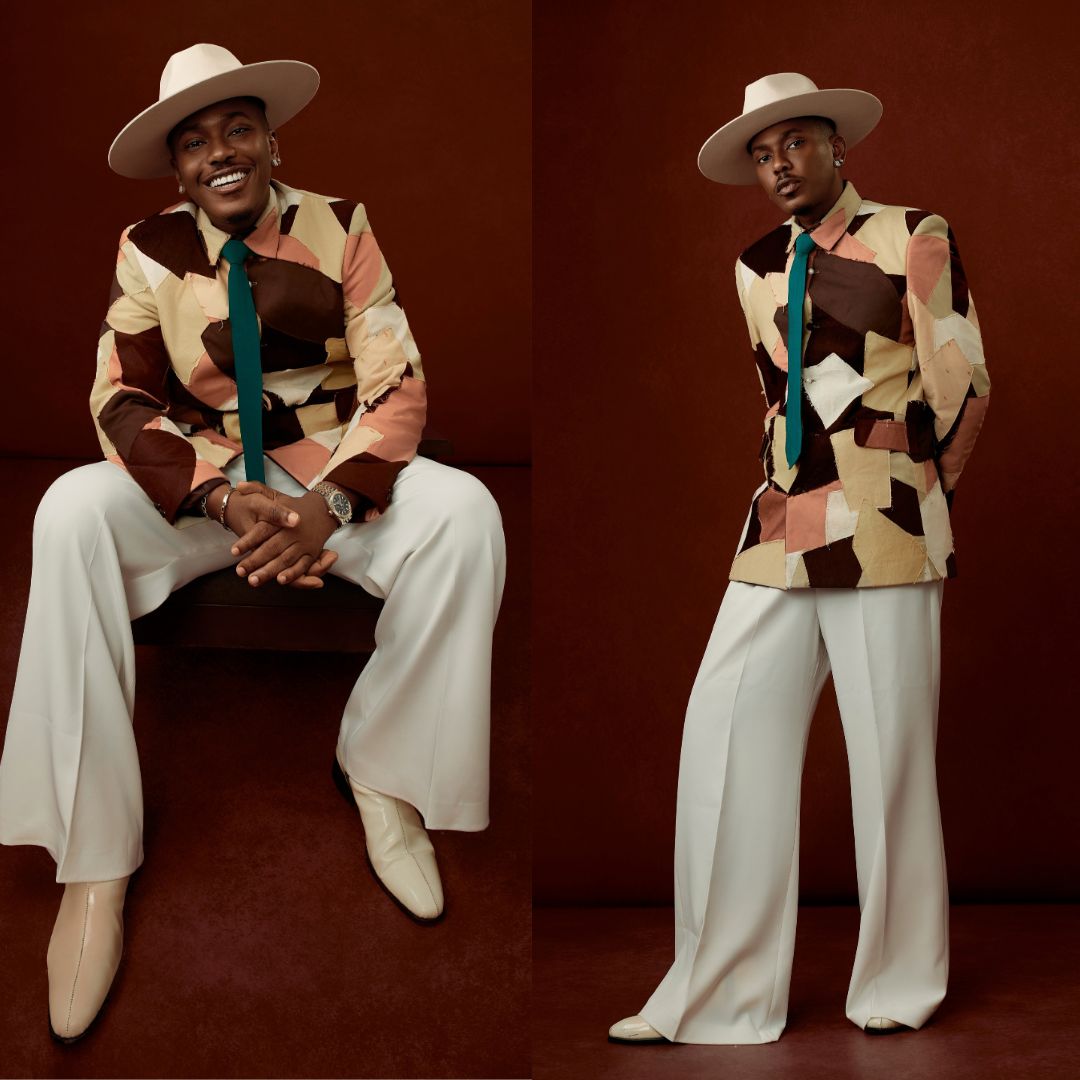 Timini Egbuson wearing an earthy patchwork suit jacket, teal tie, wide-leg trousers, and a fedora at the Starlomo premiere.