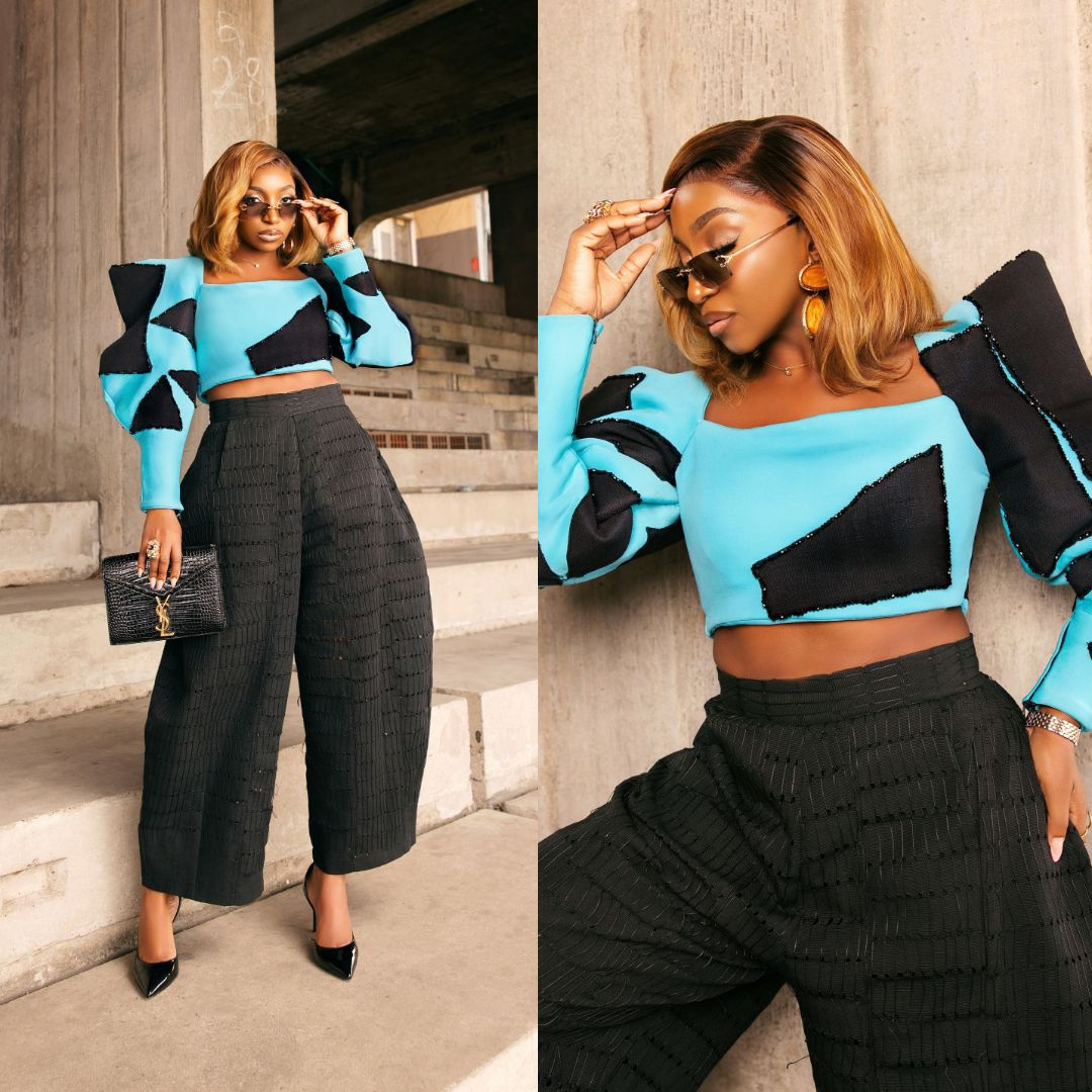 Omowunmi Dada wearing a sky-blue long-sleeve crop top with exaggerated black shoulder pads and black wide-leg trousers.