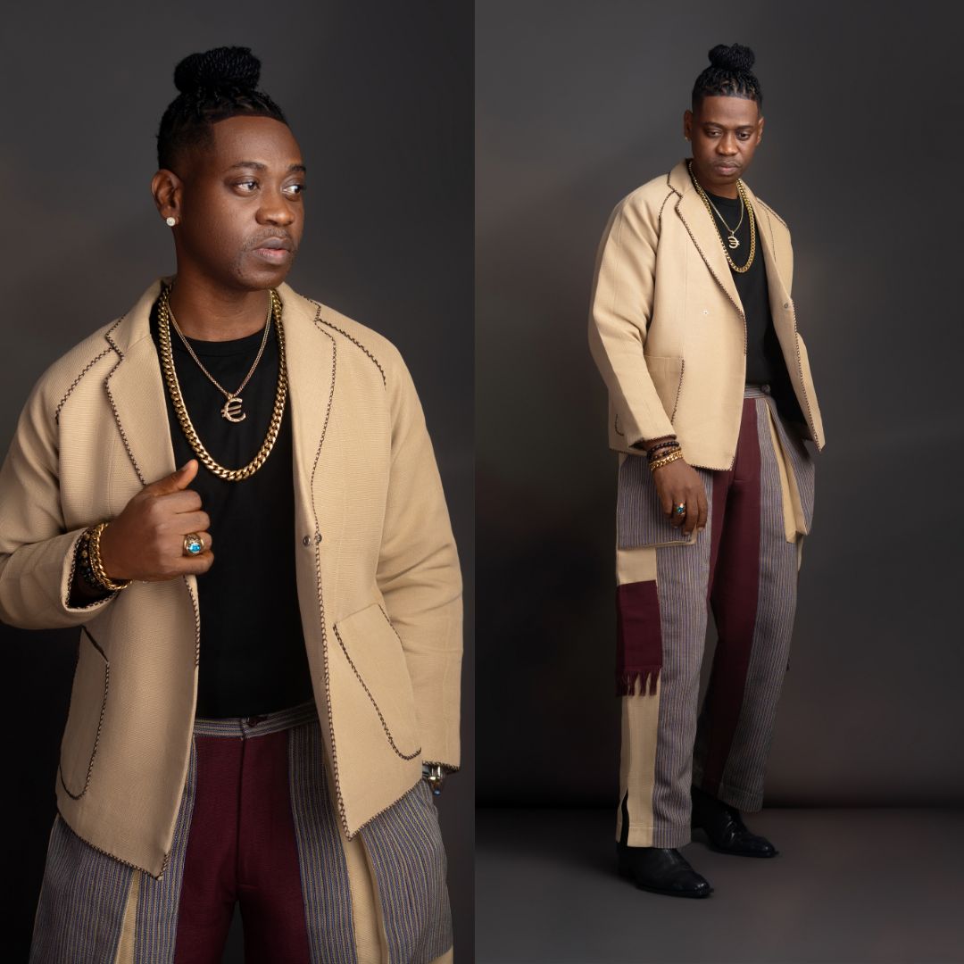Lateef Adedimeji wearing a beige stitched jacket, gold chains, and striped patchwork trousers at the Starlomo premiere.