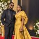 Couple on the red carpet wearing a mustard gold one-shoulder couture gown and a textured black tux for the BN 20 Gala High Fashion Icon dress code.
